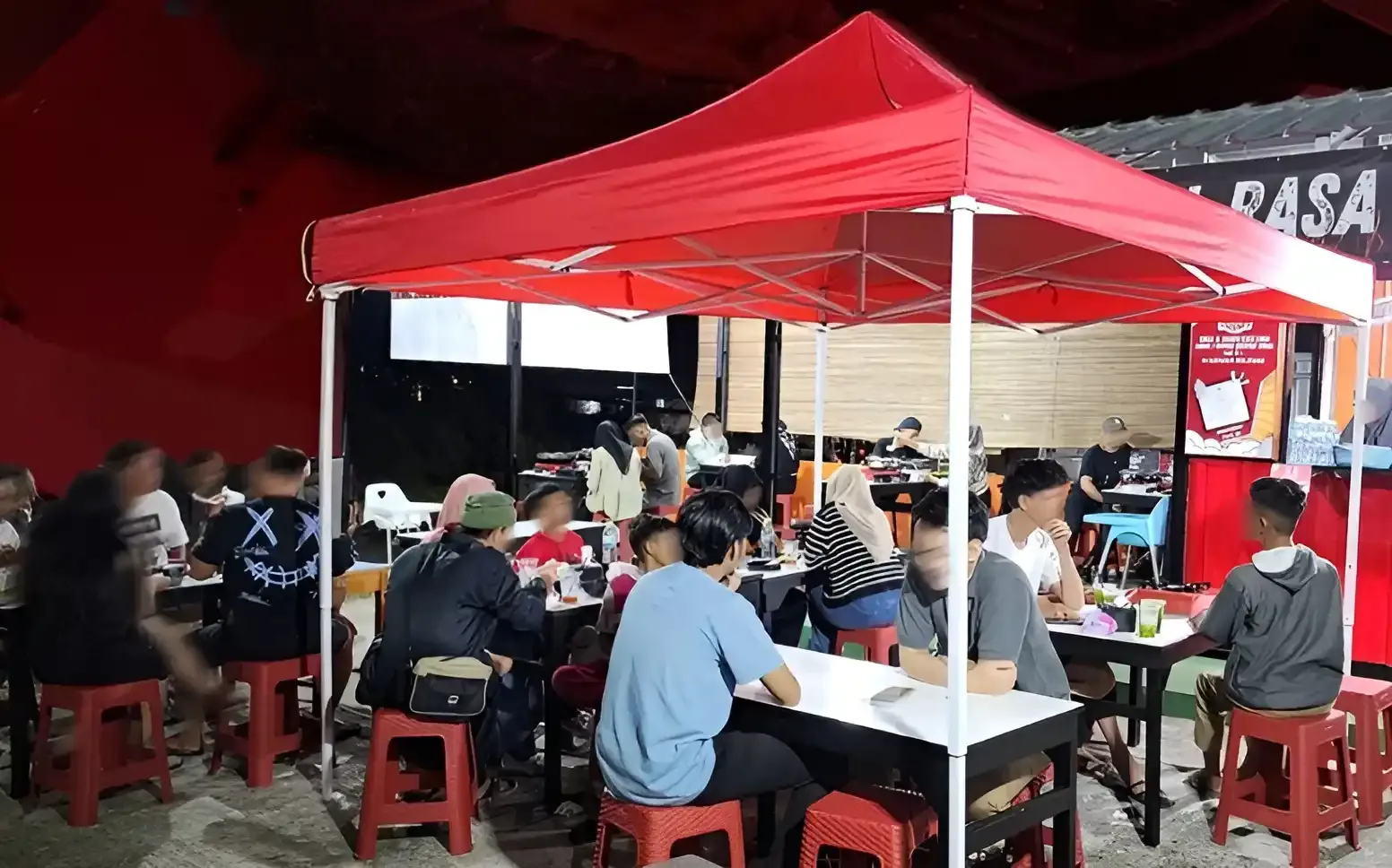 Pelanggan makan di bawah tenda merah dan bangku plastik